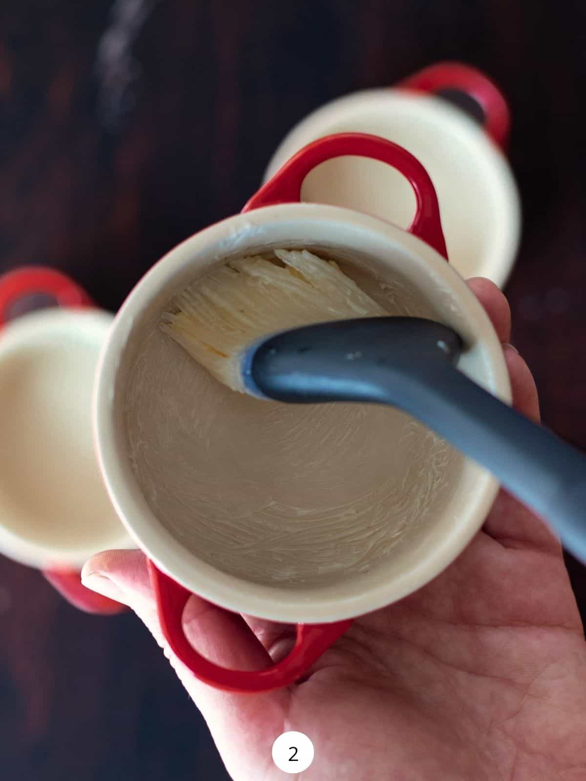Using a pastry brush to butter the cocottes.