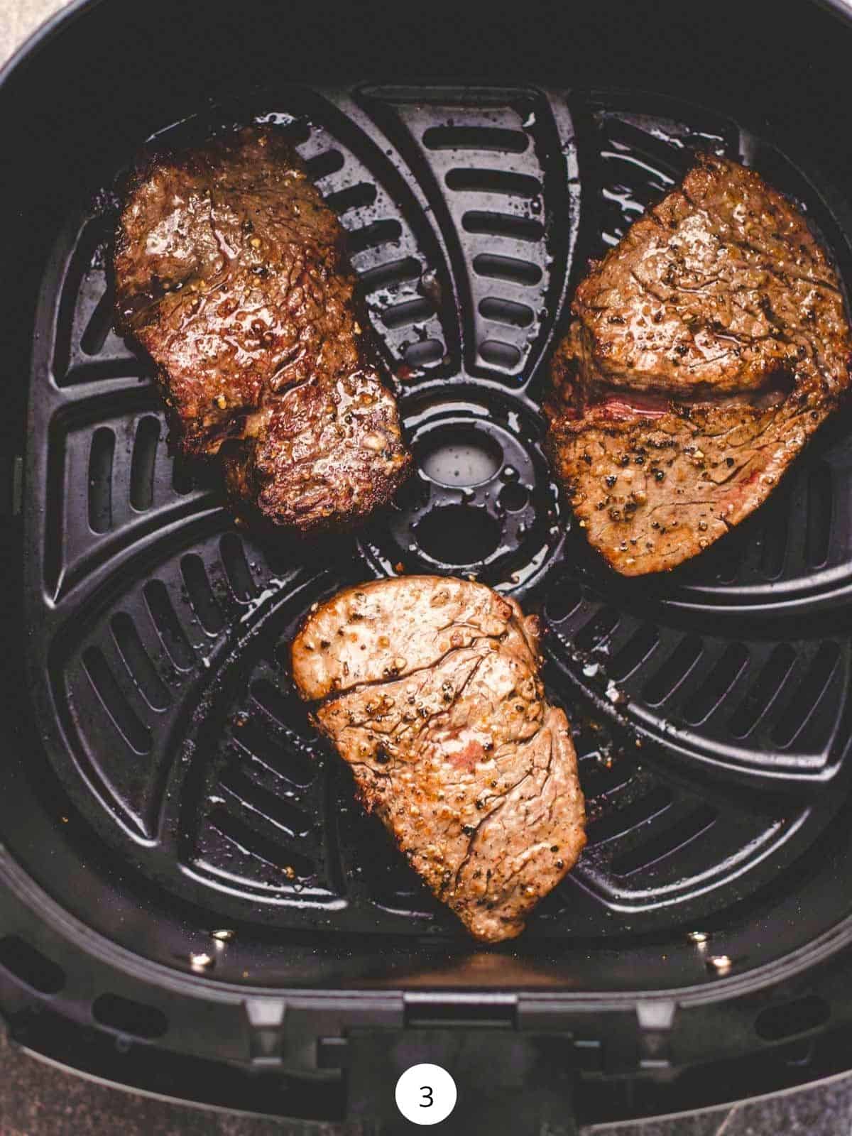 Three cooked filet mignons inside of an air fryer basket.