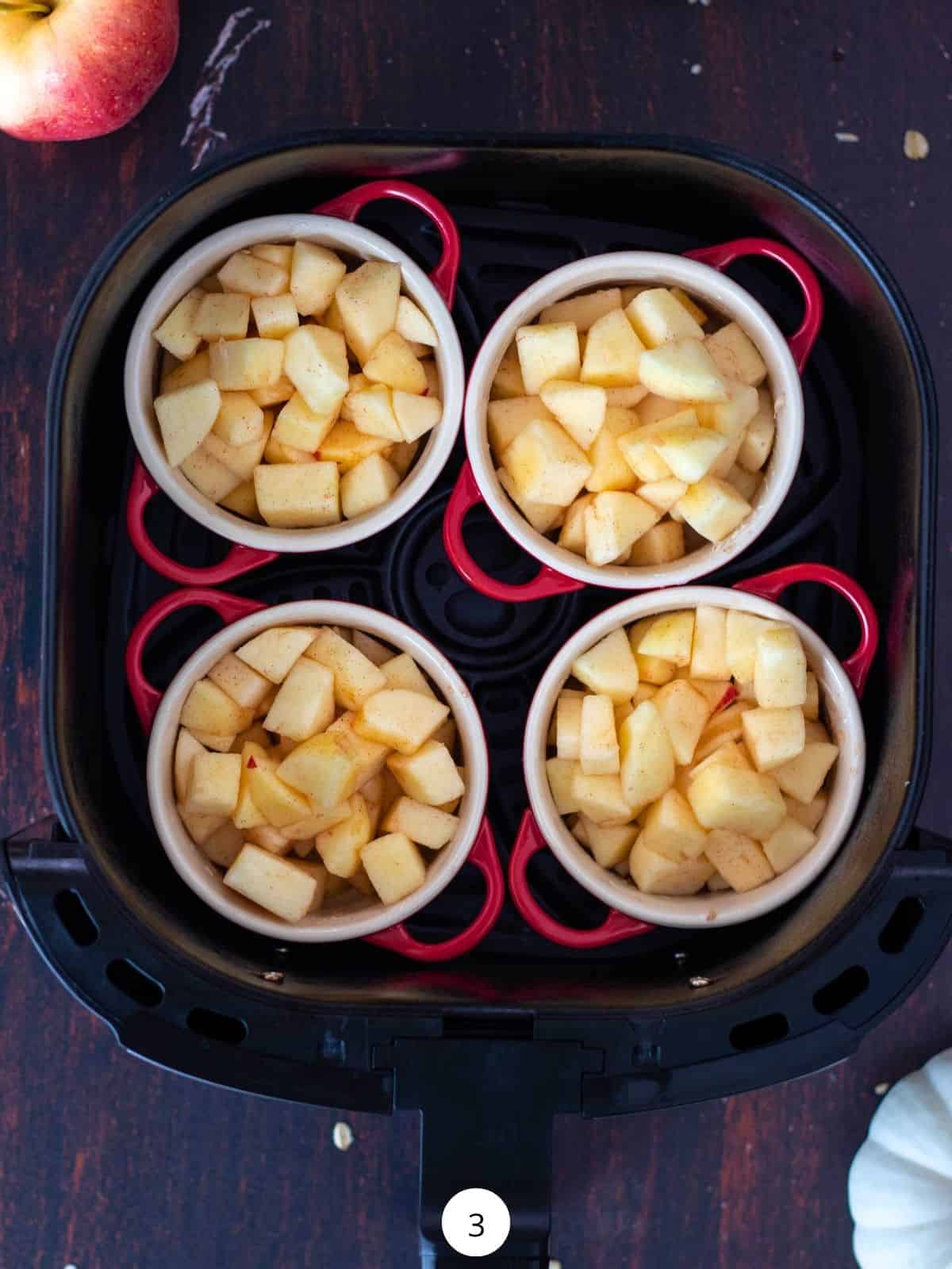 Cocottes filled with diced apples inside of an air fryer basket.