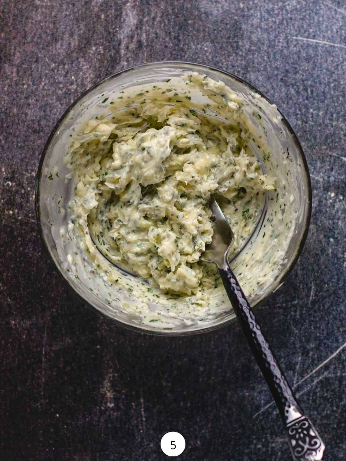 Mixing garlic-herb butter in a small glass bowl with a fork.